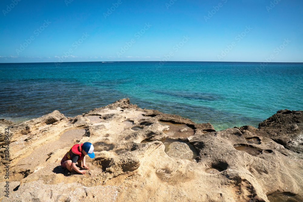 A boy looks in tide pools at edge of sea