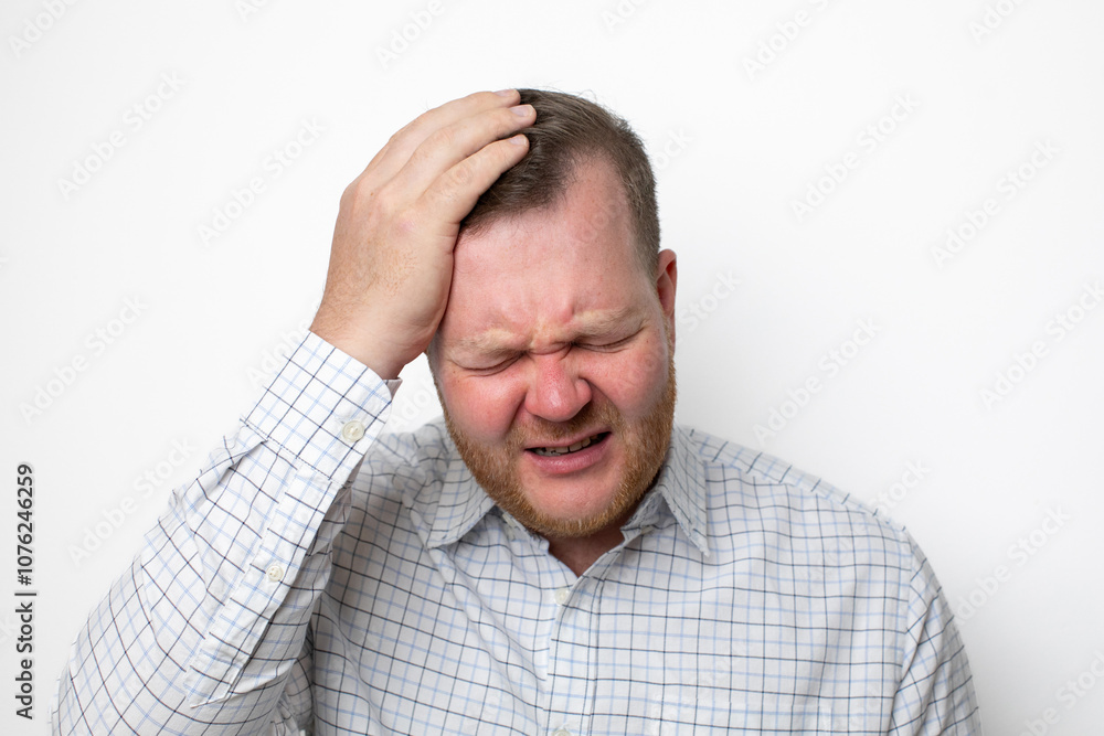 A Caucasian man in a plaid shirt holds his head in pain, representing the concept of stress and headaches A Caucasian man in a plaid shirt holds his head in pain, representing the concept of stress and headaches