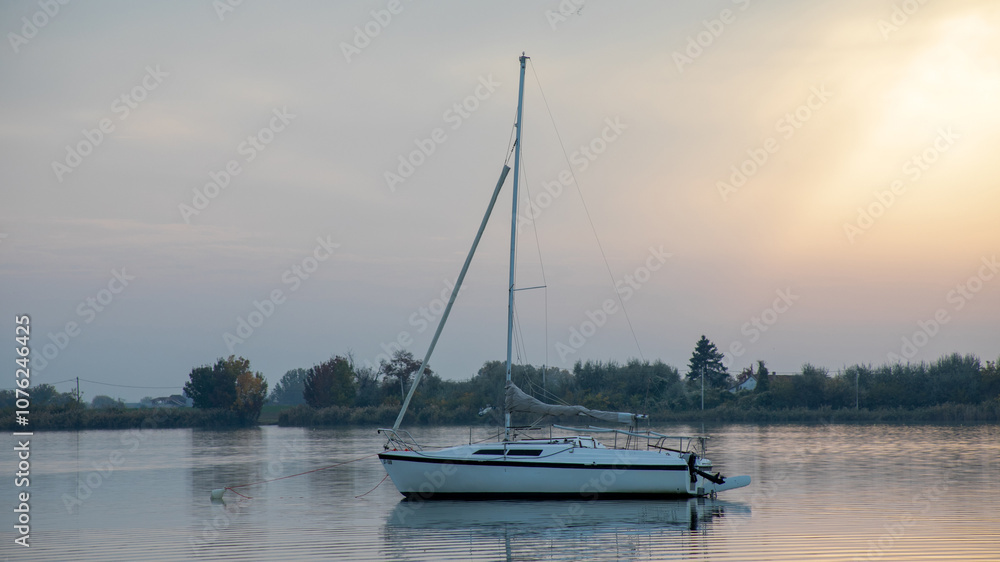 A tranquil sailboat floats on a serene lake at sunset, embodying relaxation and escape from daily stress A tranquil sailboat floats on a serene lake at sunset, embodying relaxation and escape from daily stress