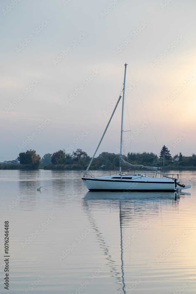 A serene sailboat floats on a tranquil lake at sunrise, symbolizing relaxation and peaceful summer getaways A serene sailboat floats on a tranquil lake at sunrise, symbolizing relaxation and peaceful summer getaways