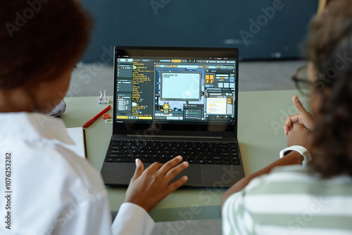 Over shoulder view of two kids using laptop in school classroom together with playful IT programming lesson on screen copy space photo