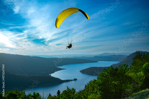 Bild auf Leinwand Paraglider with Yellow Canopy Soaring Over Lake Annecy on a Sunny Summer Day - T