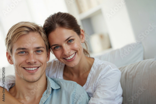 Portrait of happy smiling young couple relaxing in sofa at home and looking at camera