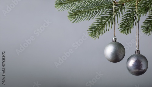 Hanging glass gray Christmas balls and pine branches on a neutral gray background with copy space