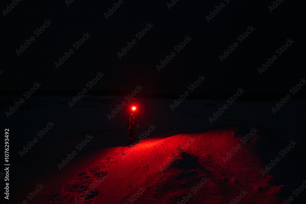 A Person in the Snow Shining a Red Flashlight in the Dark