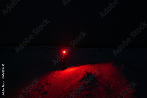 Obraz na płótnie A Person in the Snow Shining a Red Flashlight in the Dark w salonie
