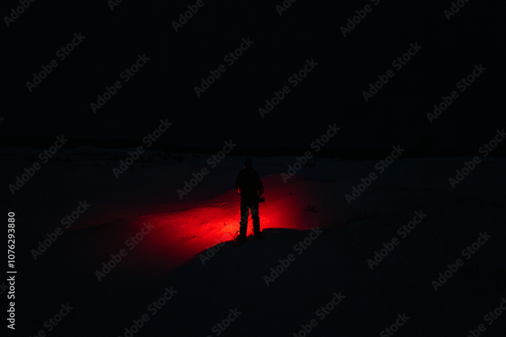 A Person in the Snow Shining a Red Flashlight in the Dark