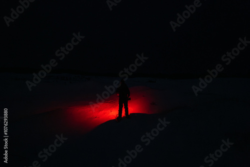 Obraz na płótnie A Person in the Snow Shining a Red Flashlight in the Dark w salonie