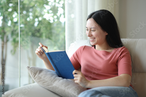 Happy asian woman reading a paper book at home