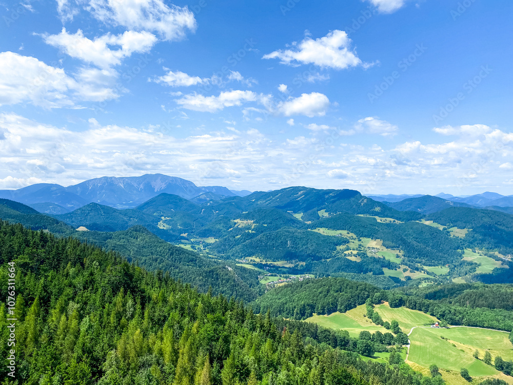 Obraz premium A stunning panoramic view of verdant hills, expansive valleys, and majestic mountains under a bright blue sky with soft, scattered clouds. This serene landscape captures the untouched beauty of nature