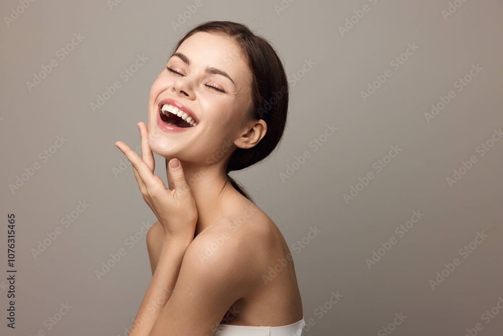 Smiling young woman with hands on face looking at camera on gray background Smiling young woman with hands on face looking at camera on gray background