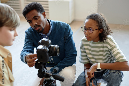 Φωτογραφία Portrait of African American man as male teacher helping children setting up vid