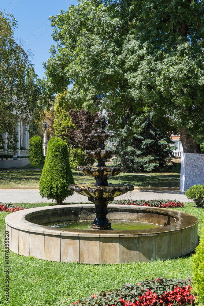 Lower park of Kislovodsk resort park. Cascade fountain in classic style. Water pours into pool through cascade of five bowls. Around fountain there are flower beds and trimmed evergreens. Topiary ar Lower park of Kislovodsk resort park. Cascade fountain in classic style. Water pours into pool through cascade of five bowls. Around fountain there are flower beds and trimmed evergreens. Topiary ar