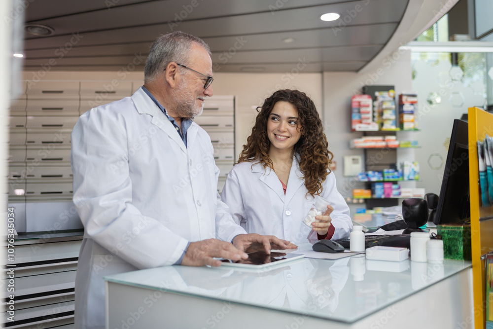 Happy pharmacist discussing over medicines with colleague at desk Happy pharmacist discussing over medicines with colleague at desk