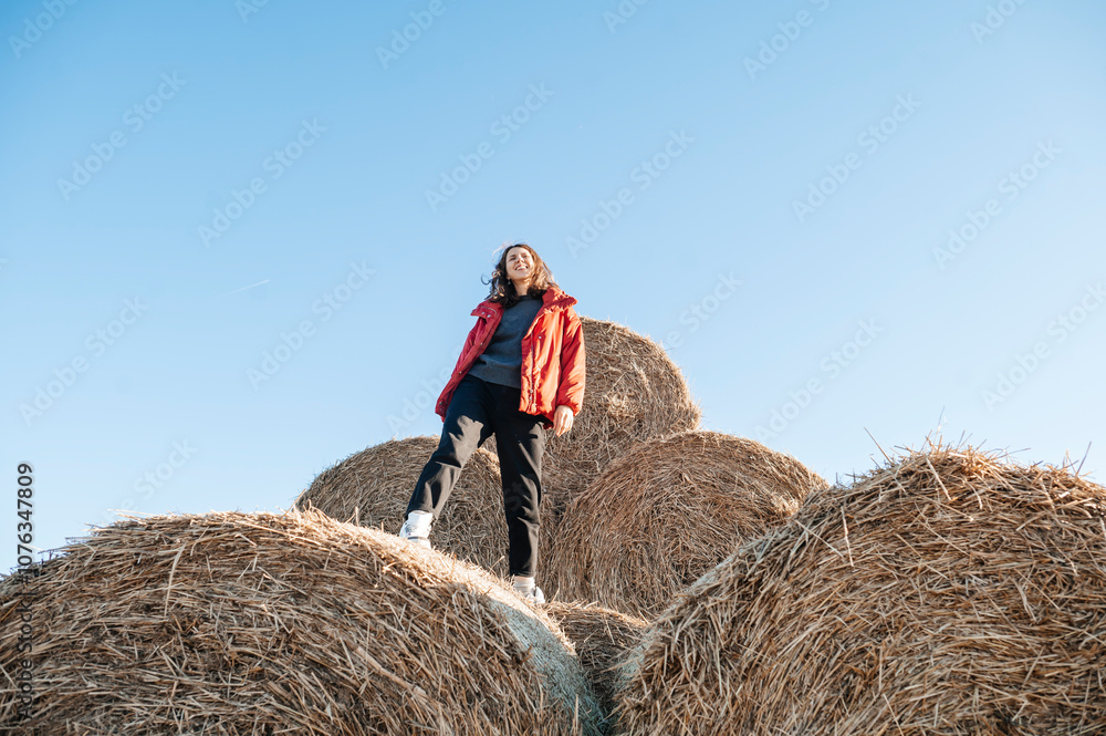 Mature woman standing on hay bale under blue sky