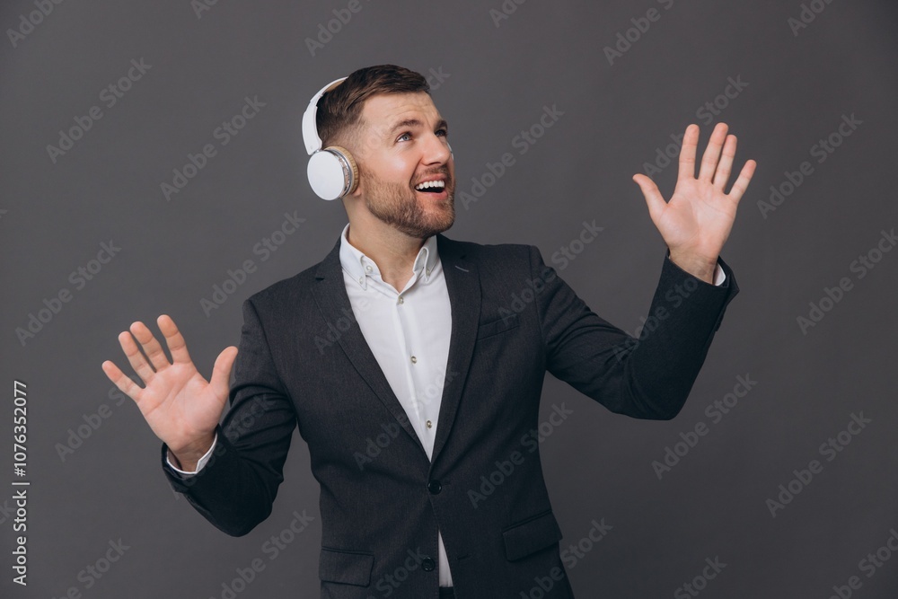 A happy smiling bearded businessman in a suit is dancing and singing attentively listening to headphones against a gray studio background A happy smiling bearded businessman in a suit is dancing and singing attentively listening to headphones against a gray studio background