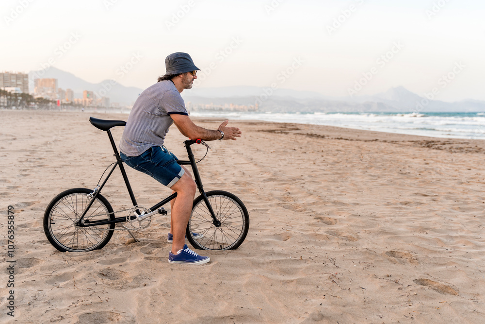 Mature man with bicycle, sitting on the beach, watching the sea Mature man with bicycle, sitting on the beach, watching the sea