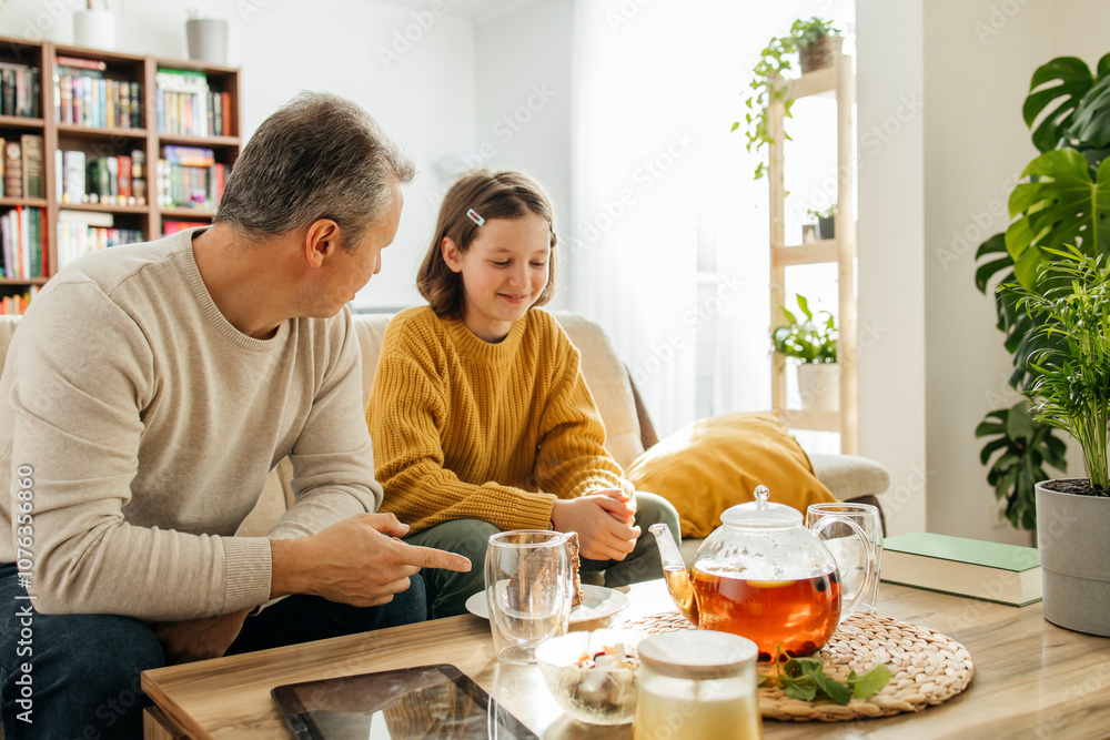 Father having tea with happy daughter sitting on sofa at home Father having tea with happy daughter sitting on sofa at home