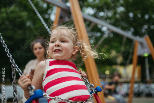 Little toddler girl and mother have fun at playground swinging on a swing photo