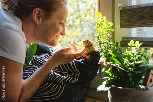 Smiling woman petting orange colored bearded dragon at home photo