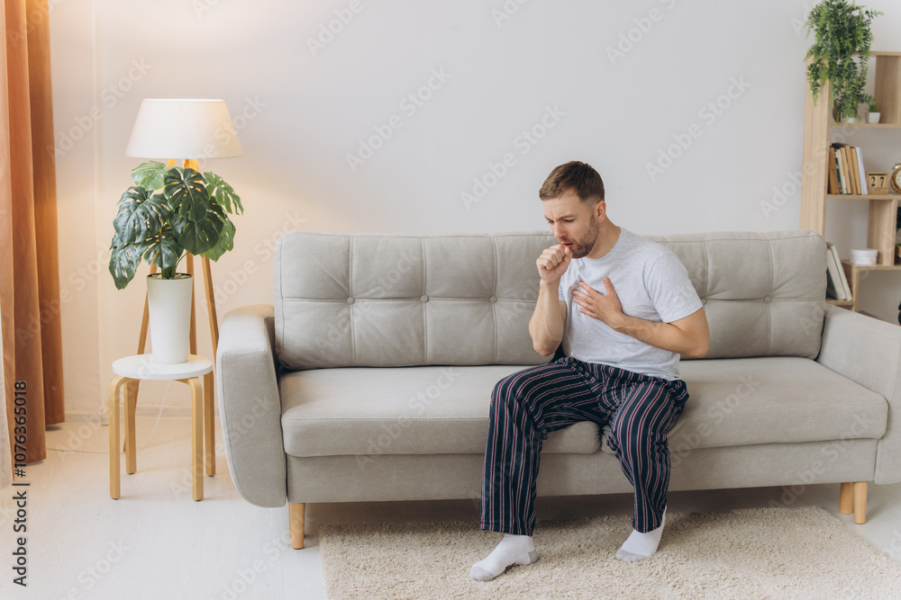 Sick man holding his chest in pain while coughing in the living room. Sore throat and cough, man with lung pain at home, health problems concept Sick man holding his chest in pain while coughing in the living room. Sore throat and cough, man with lung pain at home, health problems concept