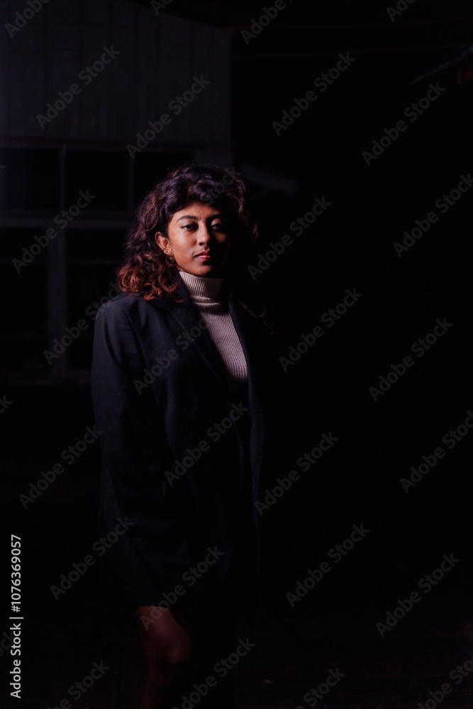 A woman wearing a black jacket and white shirt stands in a dimly lit room. She is the main focus of the image, and her outfit is the most prominent detail A woman wearing a black jacket and white shirt stands in a dimly lit room. She is the main focus of the image, and her outfit is the most prominent detail