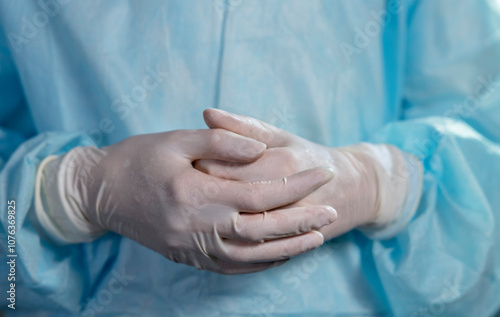 Doctor with hands clasped wearing white surgical gloves