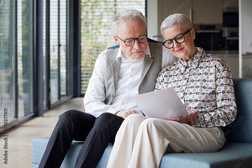 Senior couple sitting on couch at home reading document Senior couple sitting on couch at home reading document