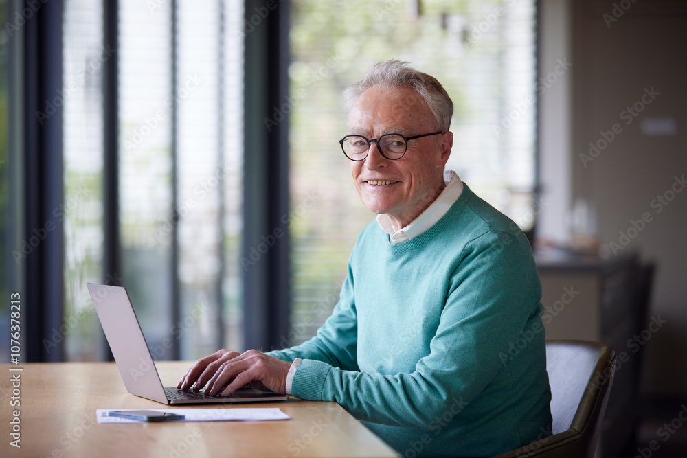 Portrait of smiling senior man using laptop at table at home