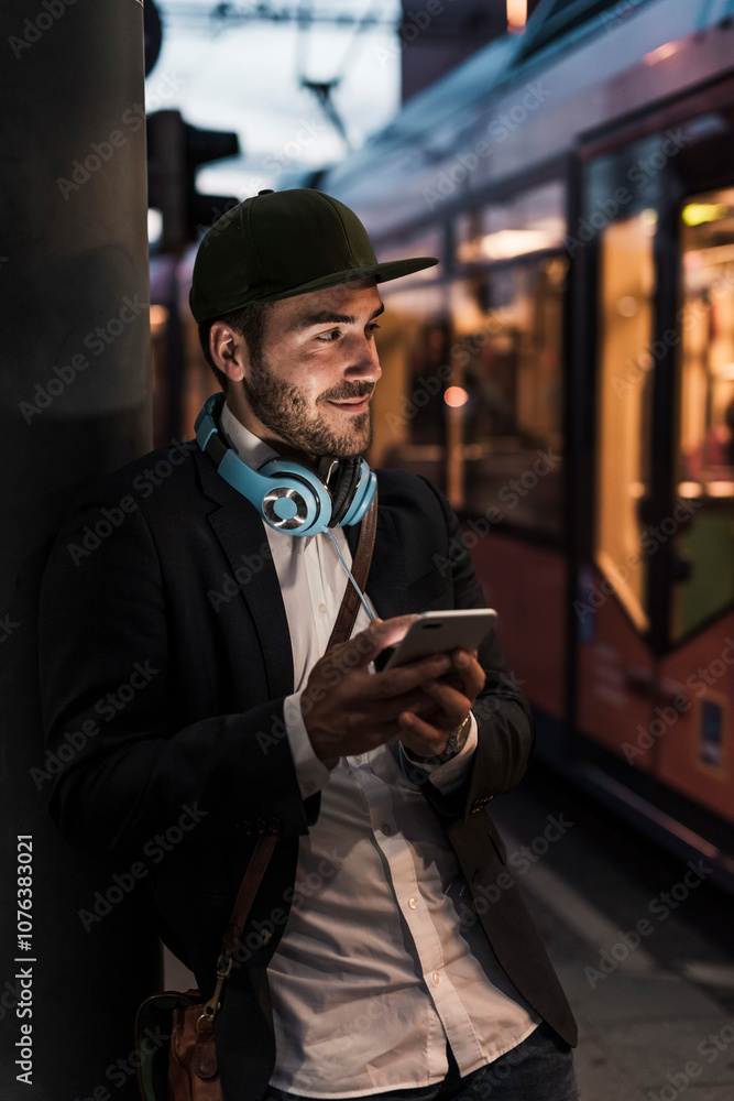 Smiling young businessman holding mobile phone and standing at railroad station Smiling young businessman holding mobile phone and standing at railroad station