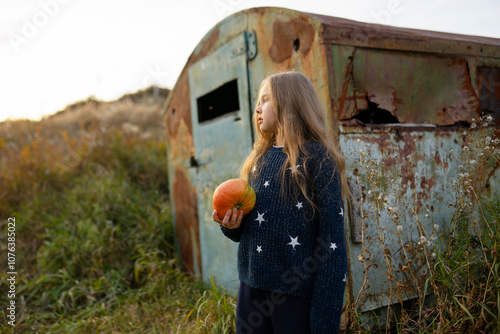 Blond girl holding pumpkin near abandoned vehicle photo