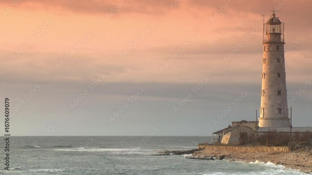 A weathered lighthouse stands along the coastline during a serene sunset. The sky glows with soft orange and pink hues, casting warm light over the scene as gentle waves reach the shore. A weathered lighthouse stands along the coastline during a serene sunset. The sky glows with soft orange and pink hues, casting warm light over the scene as gentle waves reach the shore.