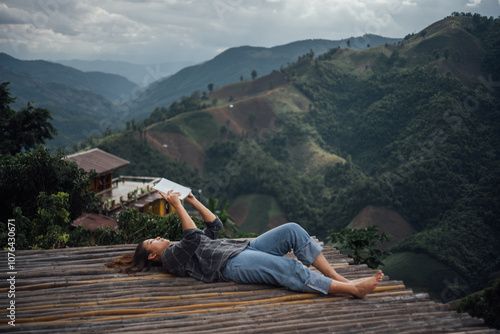 a woman lay down on a bamboo floor and reading a book in mountain landscape in her travel trip