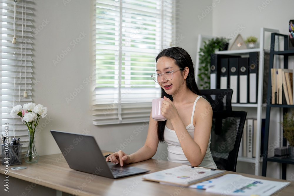 Asian freelancer woman drinking coffee and working on laptop at home Asian freelancer woman drinking coffee and working on laptop at home