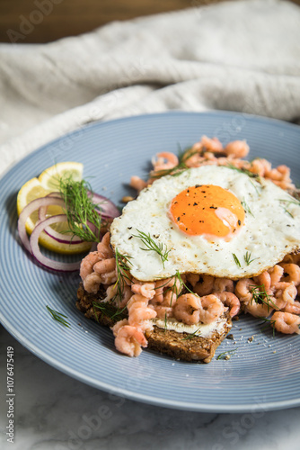 Norddeutsche Friesisches Krabbenbrot mit  Nordseekrabben  Spiegelei, Brot, Butter, Zitrone, rote Zwiebel und Dill auf blau Porzellan Teller, Serviette und hell Marmor Hintergrund