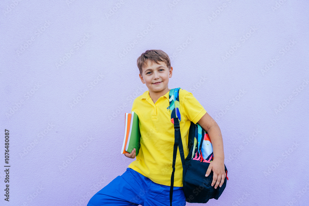 Smiling school boy with backpack and books against purple wall Smiling school boy with backpack and books against purple wall