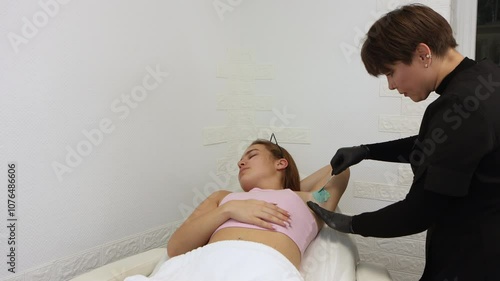 Medical female master of depilatioin doing procedure of epilation underarm waxing treatment in a beauty salon. Blue color of wax