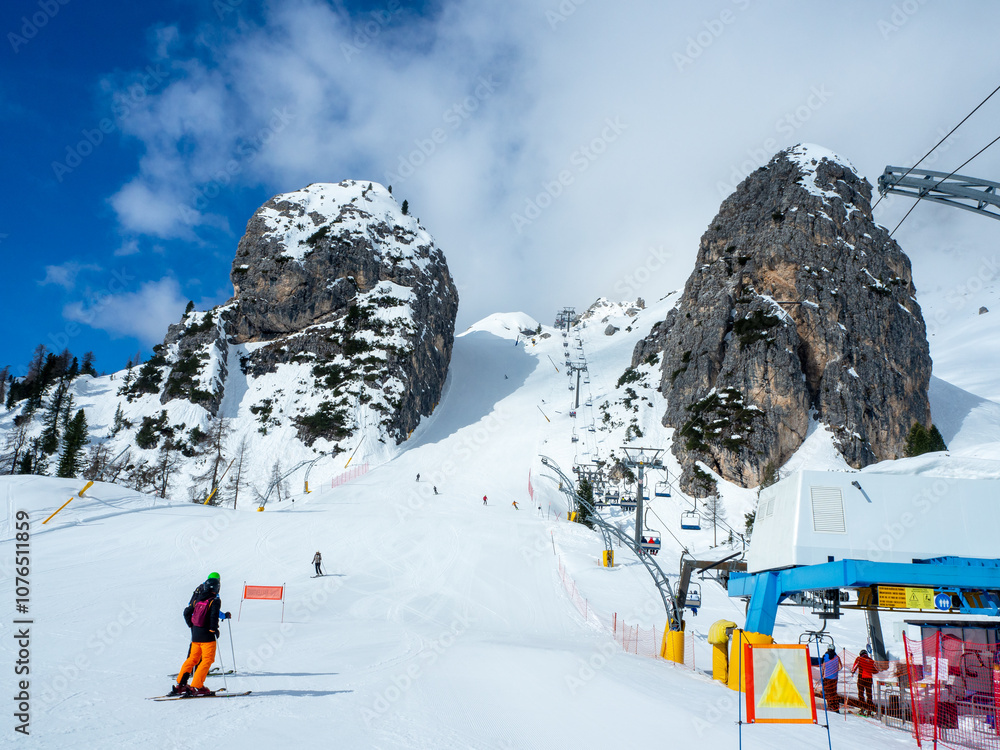 Olympic downhill ski run Olimpia 1 in Cortina d’Ampezzo in Dolomites, Italy. The steepest part between big rocks. Ski lift and unrecognizable skiers. Slope often used for Alpine ski World Cup races