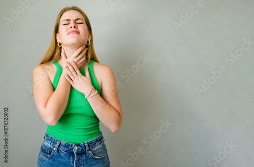 Young woman standing with her eyes closed, clutching her neck in agony photo