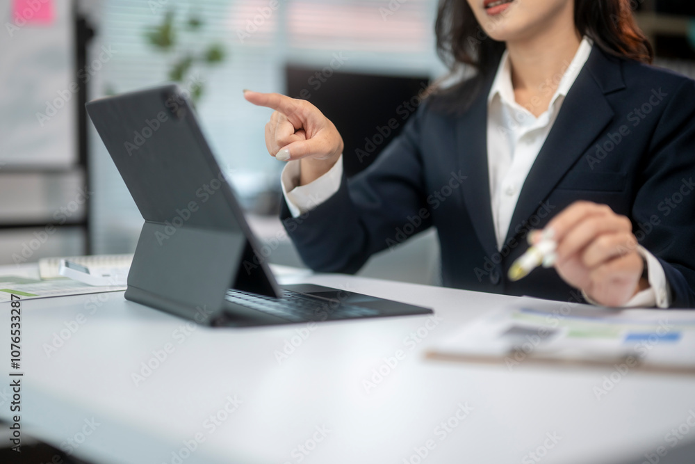 A woman in a business suit is pointing at a tablet on a desk A woman in a business suit is pointing at a tablet on a desk