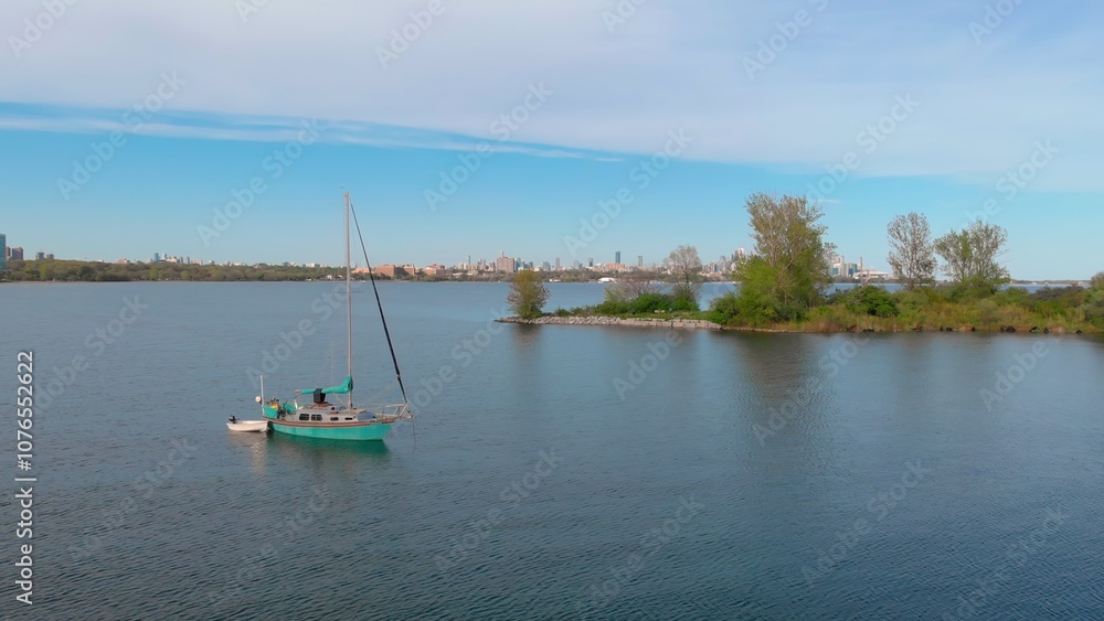 Fototapeta premium Drone view of yacht anchored on calm lake Ontario waters with Toronto skyline in background. Scene captures peaceful blend of nature and city, showcasing freedom and serenity amidst urban energy.