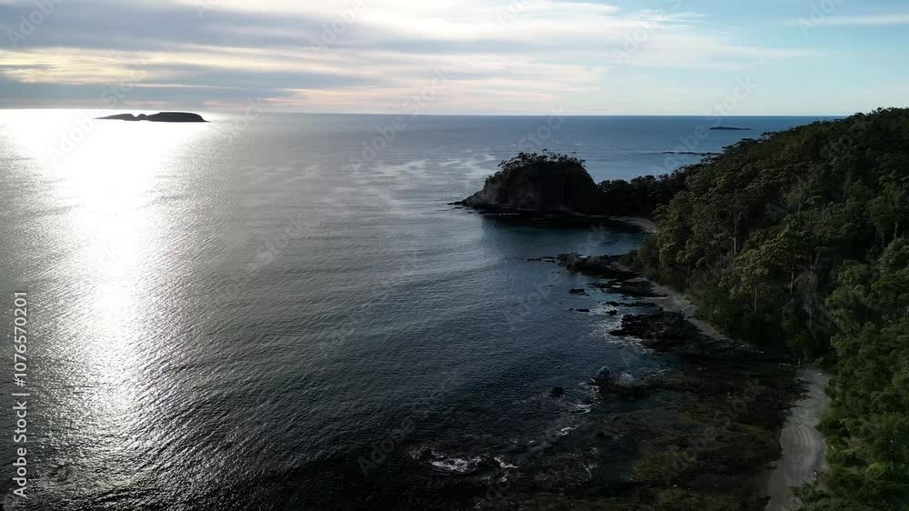 Drone view of sunlit blue waters and lush, forested shore under cloudy sky in Surf Beach, Australia Drone view of sunlit blue waters and lush, forested shore under cloudy sky in Surf Beach, Australia
