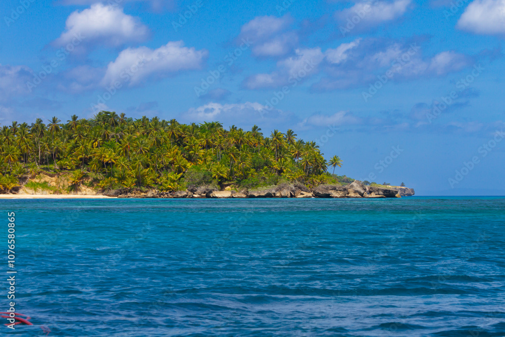 A serene coastal scene showcases a turquoise sea gently lapping against a rugged cliff topped with lush greenery. In the distance, a solitary rock formation rises from the water under a clear blue sky A serene coastal scene showcases a turquoise sea gently lapping against a rugged cliff topped with lush greenery. In the distance, a solitary rock formation rises from the water under a clear blue sky