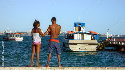 ITAPARICA, BAHIA STATE, BRAZIL: young african-american couple standing up together and watching Salvador de Bahia skyline, from the boat pier, across 