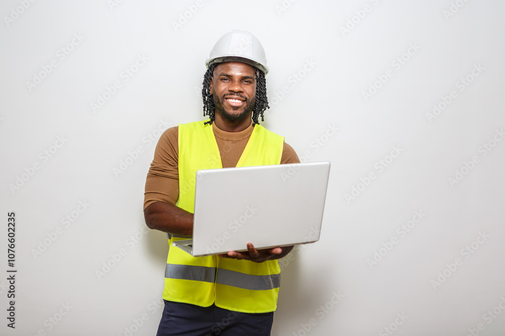 Construction worker with laptop smiles while standing against a plain background in a safety vest Construction worker with laptop smiles while standing against a plain background in a safety vest