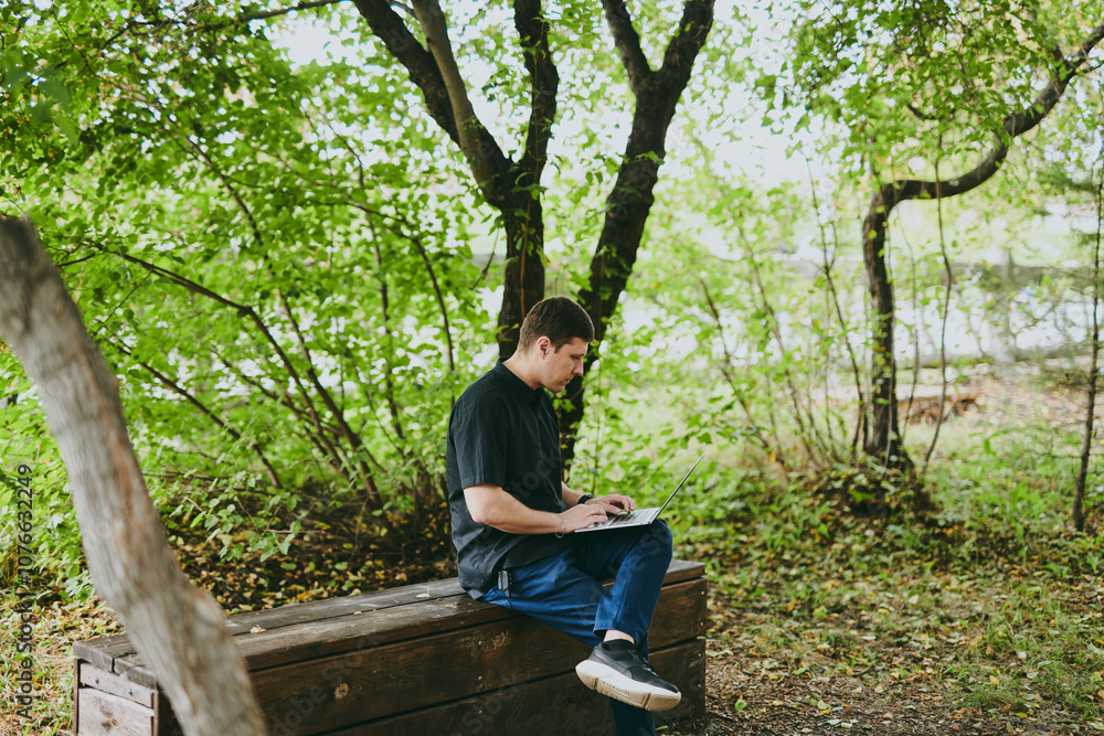 Fototapeta premium Portrait of young freelance programmer man working with laptop in forest park, software developer, IT technologies