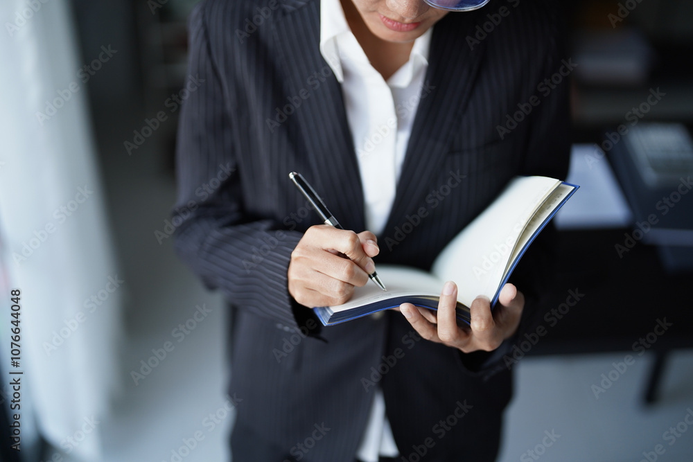 Asian businesswoman in suit standing using pen writing on notebook Asian businesswoman in suit standing using pen writing on notebook