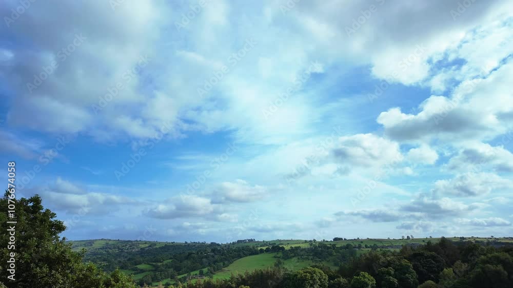 Timelapse of white clouds moving in a bright, blue sky over an English countryside landscape Timelapse of white clouds moving in a bright, blue sky over an English countryside landscape
