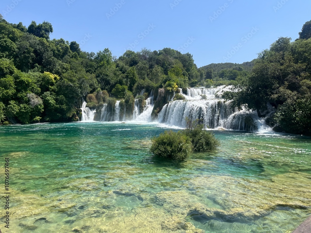 Fototapeta premium Breathtaking Waterfall Cascading into Crystal Clear Waters Surrounded by Lush Greenery