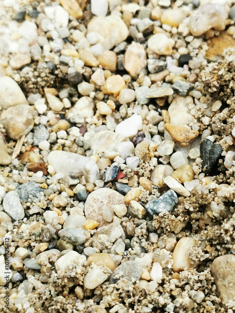 Close-up of textured pebbles and grains of sand on a beach showing natural variations in color and size during daylight Close-up of textured pebbles and grains of sand on a beach showing natural variations in color and size during daylight